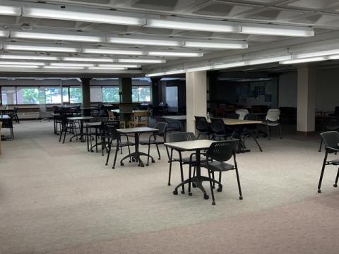 large open space with low ceilings, windows along the back, moveable tables and chairs