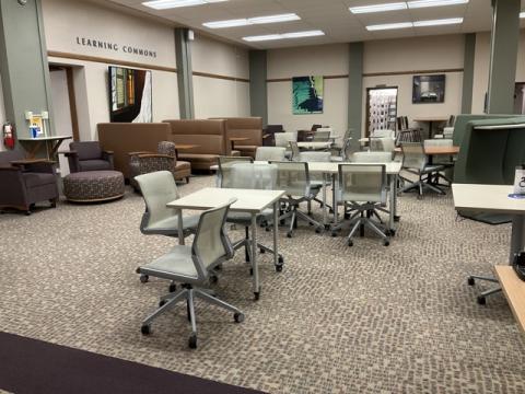 Room with tables, chairs, upholstered chairs and ottomans, booths, tall table, colorful art on the walls and "Learning Commons" on the wall