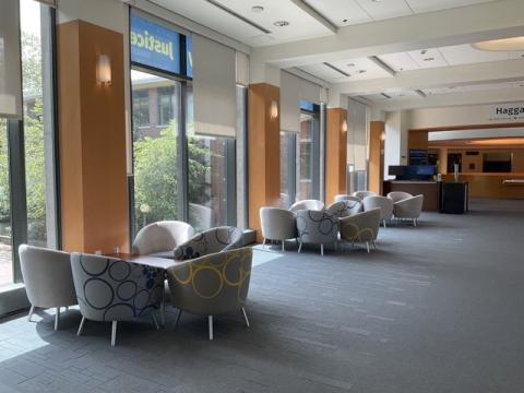Space with floor to ceiling windows, clusters of upholstered chairs with coffee tables, computers and printers at end of space