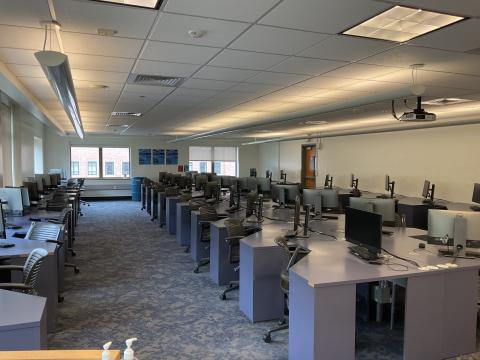 Lab with four long rows of angled desks, each with a monitor and a computer. Middle row has back-to-back desks. One row against left and right walls.