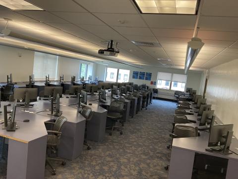 Large lab with four long rows of angled desks, each with a monitor and a computer. Middle row has back-to-back desks. One row against left and right walls.