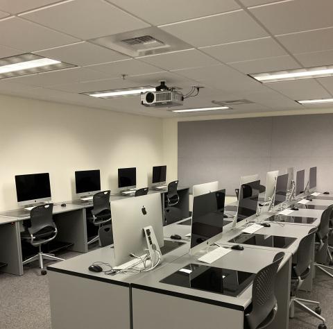 A windowless computer lab with three rows of Macs: One against the lefthand wall, two back-to-back in the center of the room.