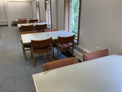 An open space with three tables, each with four chairs. Tall, narrow windows along the righthand side.