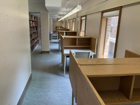 A long, open space with carrels and narrow windows along the entire righthand wall. Columns and bookstacks along the lefthand side create a very narrow walkway.