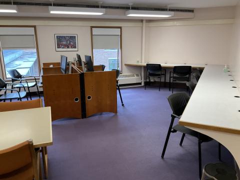 A corner with four computer monitors and windows against back wall. Long counter with chairs curves along righthand corner. Part of table on lefthand side.