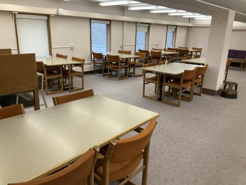 Open space with long tables surrounded by chairs on back wall and middle of room. Carrol on the back left. Windows on back wall. Columns on the right.