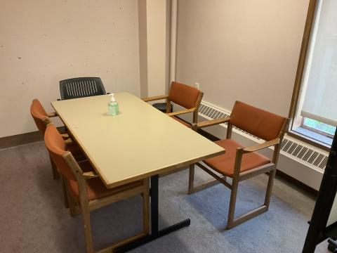 A long table surrounded by five chairs in a small space. Part of a window visible on the right.