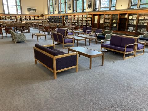 Couches and coffee tables in an open space. Bookshelves along back wall. Old reading desks on back left. Large windows above bookshelves.