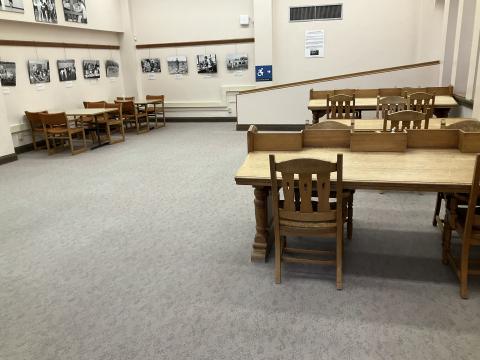 An open space with sparse furniture. Long, slanted reading desks on right. Standard long table on back left. Wheelchair ramp in background.