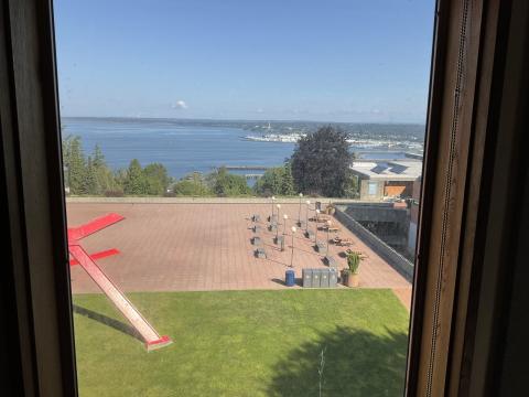 View through a window. The bay is visible in the distance, VU side entrance on the right. Lawn and large metal statue in foreground.