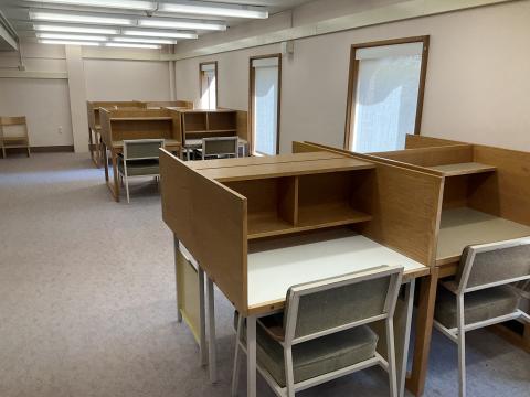 An open space with pairs of carrels back-to-back and protruding from a wall on the right. Windows in the right wall.