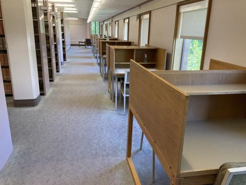 An open space with carrels lined up against the right wall. Bookstacks and columns on the left. A walkway between the carrels and books.