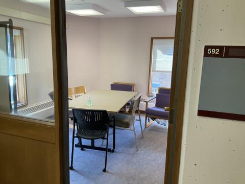 A small room viewed from through the doorway. Wall adjacent to door is windowed. Long table surrounded by chairs with windows on left and back wall.