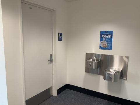 A closed door for a men's restroom on the left, water fountains on the right wall adjacent to the door.