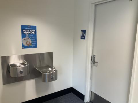 A closed door for a women's restroom on the right, water fountains on left wall adjacent to the restroom.