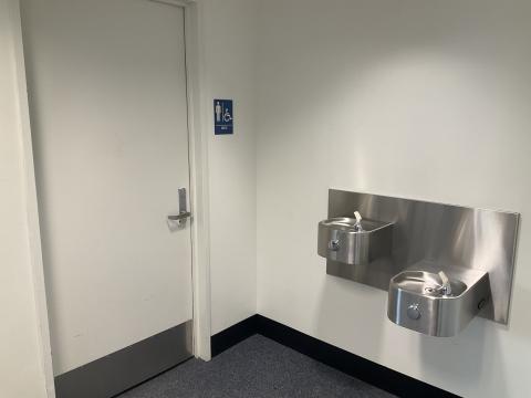 A closed door for a men's restroom on the left, water fountains on adjacent wall to the right.
