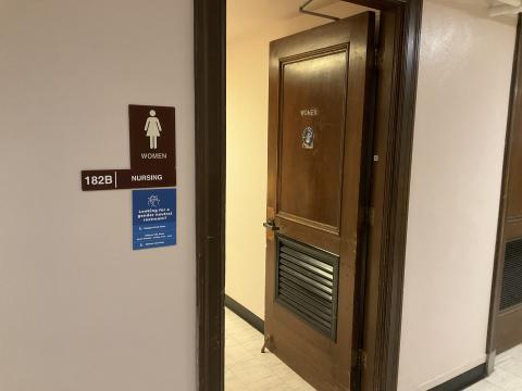 Open door into women's restroom. Signage to left of door with room number and locations of gender-neutral restrooms. 