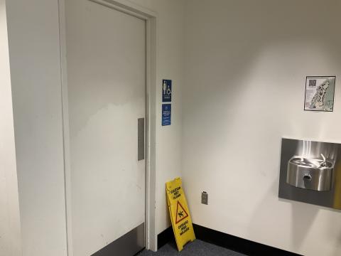 Closed door into women's restroom. Water fountain on adjacent wall to the right. Wet floor sign.