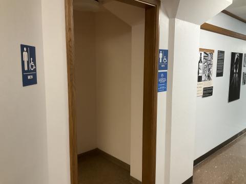 Open door into a men's restroom. Signage denoting gender to left and right of door. Photo gallery on wall past doorway.