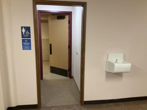 Open door to women's restroom. Signage denoting gender to left of door. Water fountain to the right of the door.