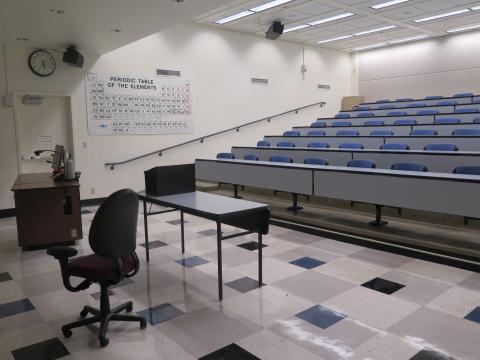 lecture hall with tiered seating, long grey tables slightly curved with blue seats.