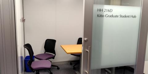 Small room seen through an open doorway. Long table with purple rolling chairs. Frosted glass label on door; HH 216D Kitto Graduate Student Hub.